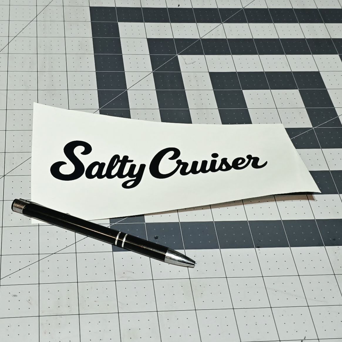 Black Salty Cruiser script decal on backing paper beside a pen