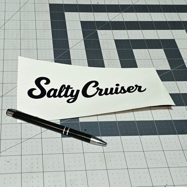 Black Salty Cruiser script decal on backing paper beside a pen
